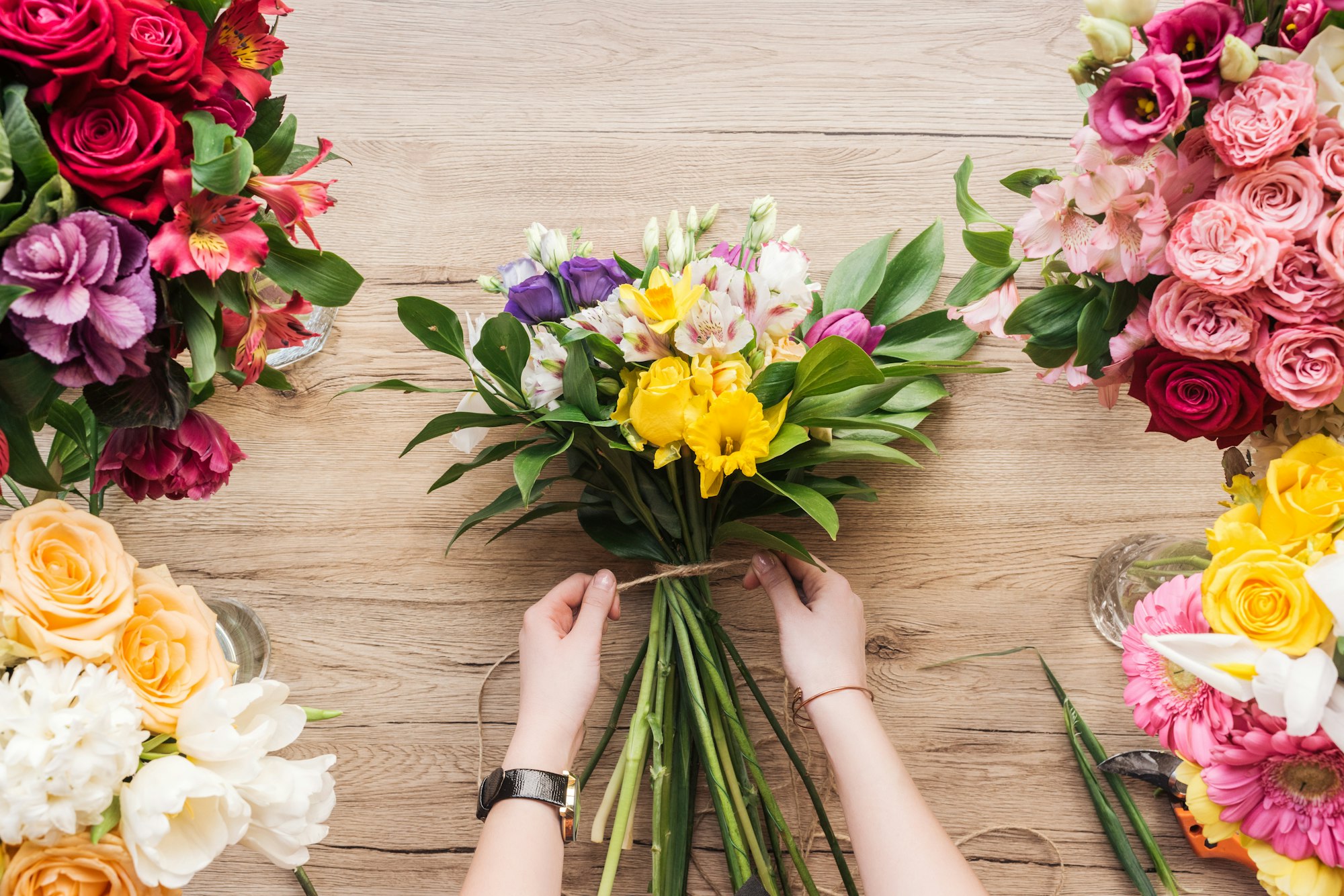 Cropped view of florist making flower bouquet on wooden surface